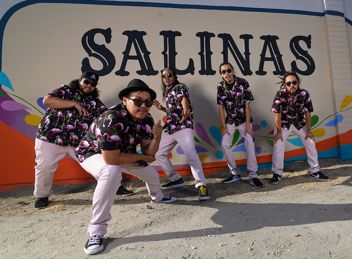 ¿Qiensave? (Quien-Sa-Be) Cumbia Urbana band that consists of five members. They are Latinx, in thirties or so,  and wear shirts with pink flamingos, light pink pants, and black and white sneakers.