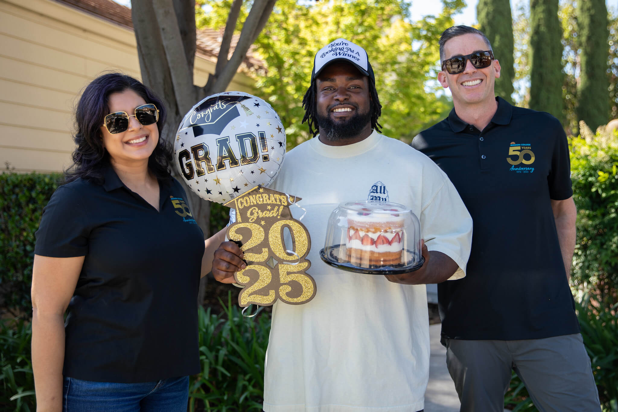 President Seher posing with graduate holding cake, sign and balloon