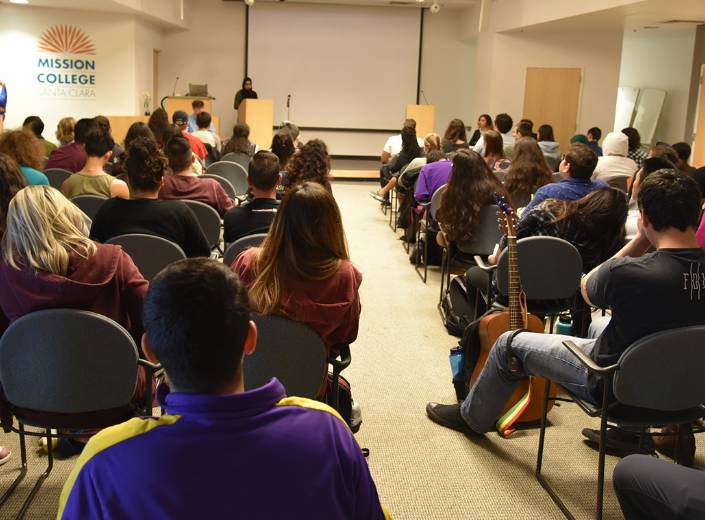 People at an event in campus. They sit in chairs facing a screen for a projector.