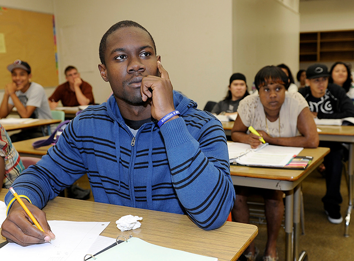 African-American make student in long-sleeved blue shirt focuses on a classroom lesson. He holds a pencil in his hand to take notes.
