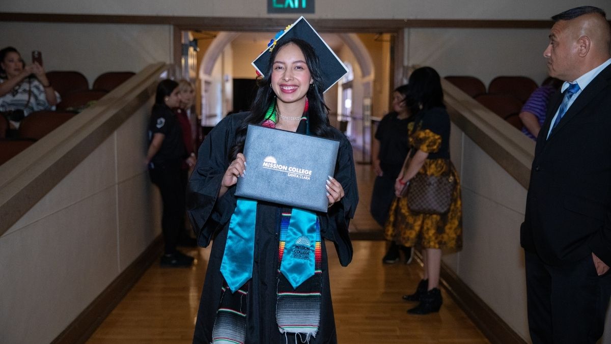 Mission College graduate smiling with diploma