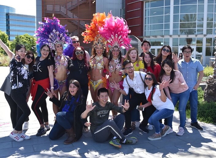 Carnivale dancers pose with group of students (male, female, various ethnic backgrounds) for an event outside on campus.