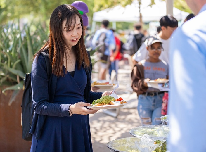 A woman in a light blue scarf and black hair is distributing oranges. "Second Harvest Food Bank" is writen in white text across a teal strip of color on the bottom of the image.